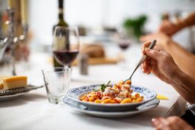 Hand of a female eating pasta sitting at dining table.