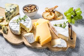 Assorted cheeses on a wooden cutting Board. Camembert, brie, Parmesan and blue cheese with grapes and walnuts