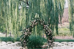 large greenery and pink floral wedding arch in front of willow tree