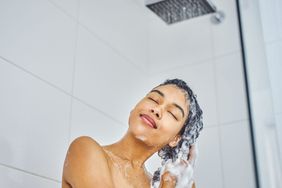 Shot of a young woman washing her hair with shampoo in the shower at home