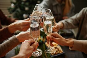 Close up of friends clinking champagne glasses while enjoying Christmas dinner together sitting by elegant dining table with candles