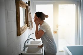 woman inspecting face bathroom mirror