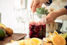 woman mixing a pitcher of cocktails with fruit at home