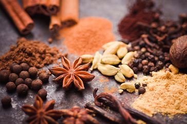 loose spices, cinnamon sticks, cloves on a neutral surface