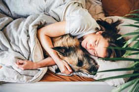woman in bed cuddling older dog