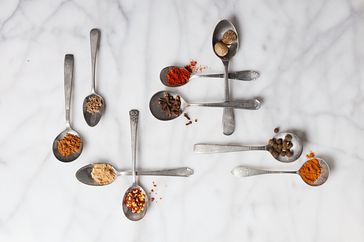 overhead view of multiple spoons with spices on marble