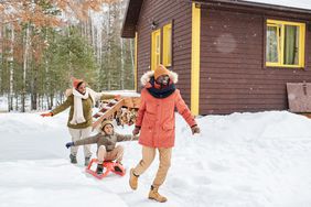 Young cheerful man having fun with his family while pulling sledge with happy boy outstretching his arms and enjoying ride