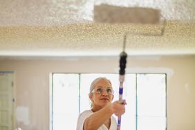 woman painting ceiling with roller brush